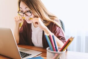 Mahasiswa sedang belajar sendiri dengan laptop dan buku di kamar