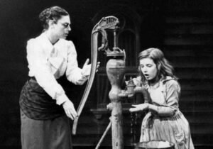 Anne Sullivan mengeja kata 'air' di tangan Helen Keller di sebuah pompa air.